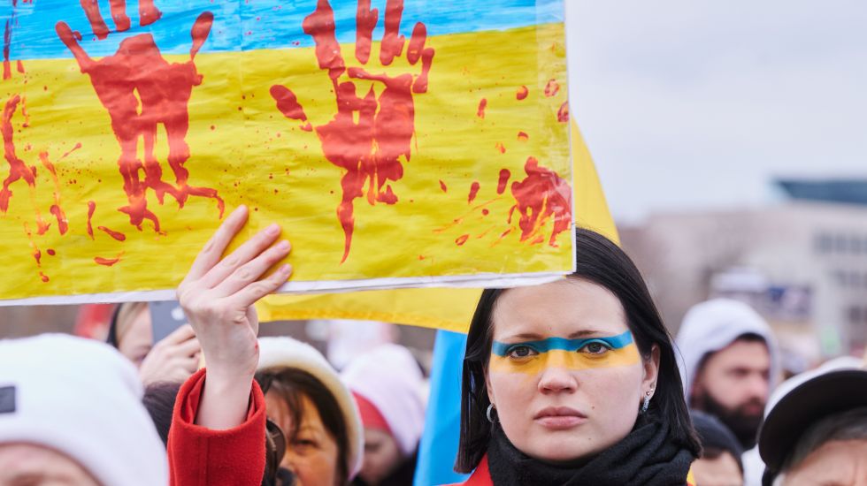 Sophia, geboren in Russland, aber bis vor kurzem in Kiew lebend, hält ein Schild auf dem rote Handabdrücke zu sehen sind. Sie protestiert zusammen mit vielen weiteren Demonstrantinnen und Demonstranten auf der Wiese vor dem Reichstagsgebäude.