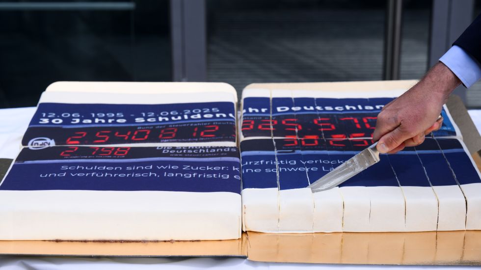 Mann schneidet einen Kuchen mit einer Schuldenuhr-Glasur an